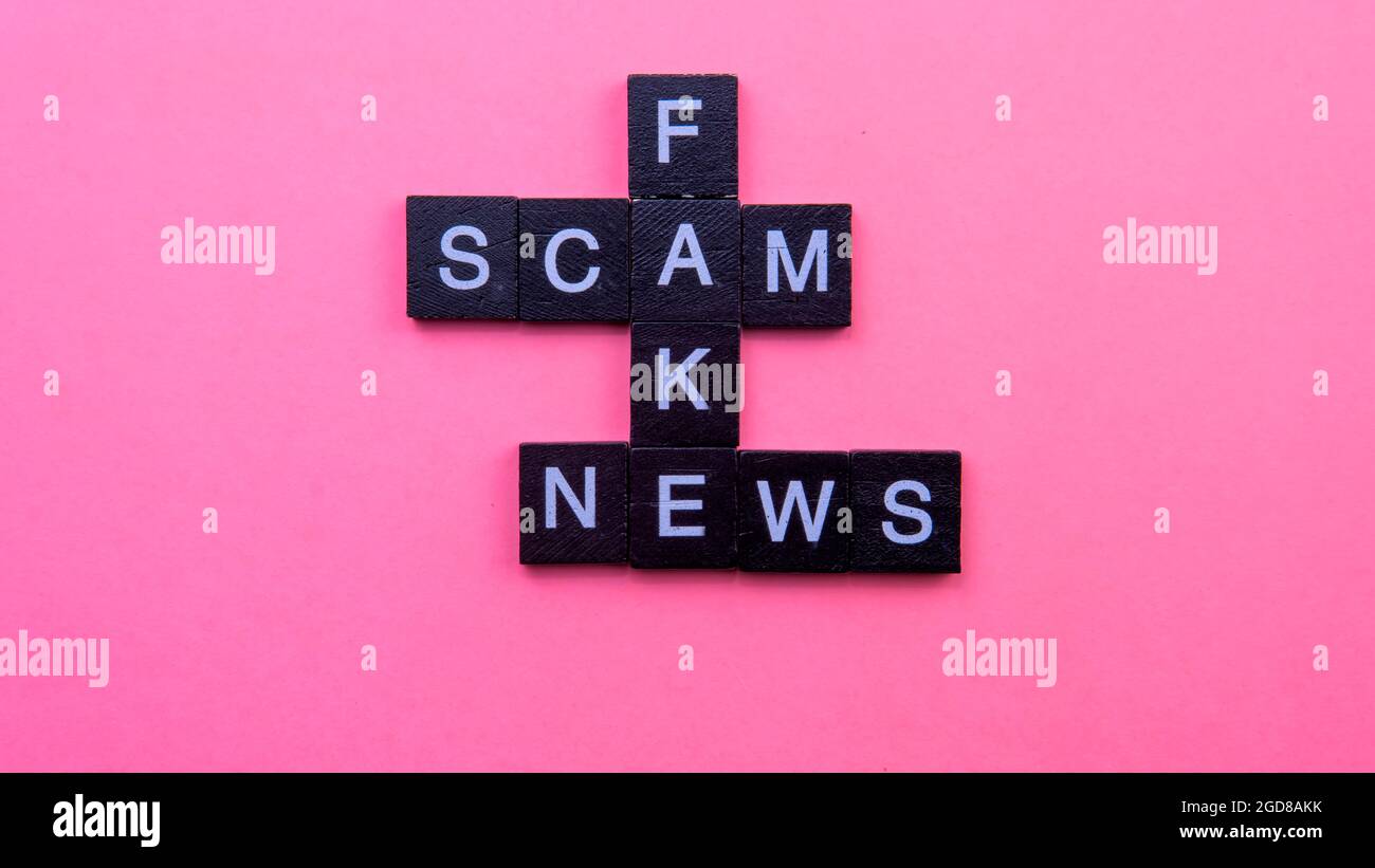 Un gruppo di piastrelle scrable che formano le notizie false di truffa di parola. Fuoco selettivo sulle piastrelle isolate su sfondo rosa Foto Stock