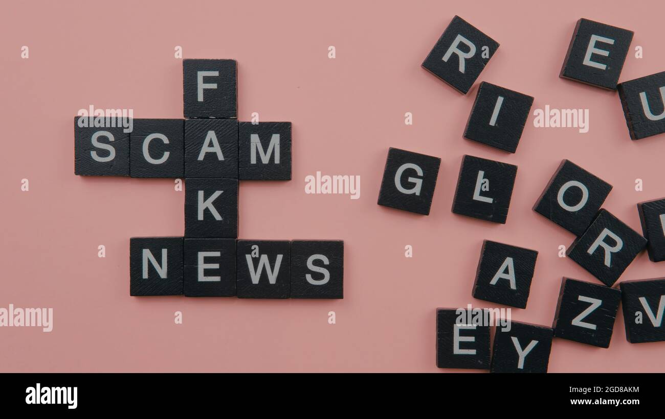 Un gruppo di piastrelle scrable che formano le notizie false di truffa di parola. Fuoco selettivo sulle piastrelle isolate su sfondo rosa Foto Stock