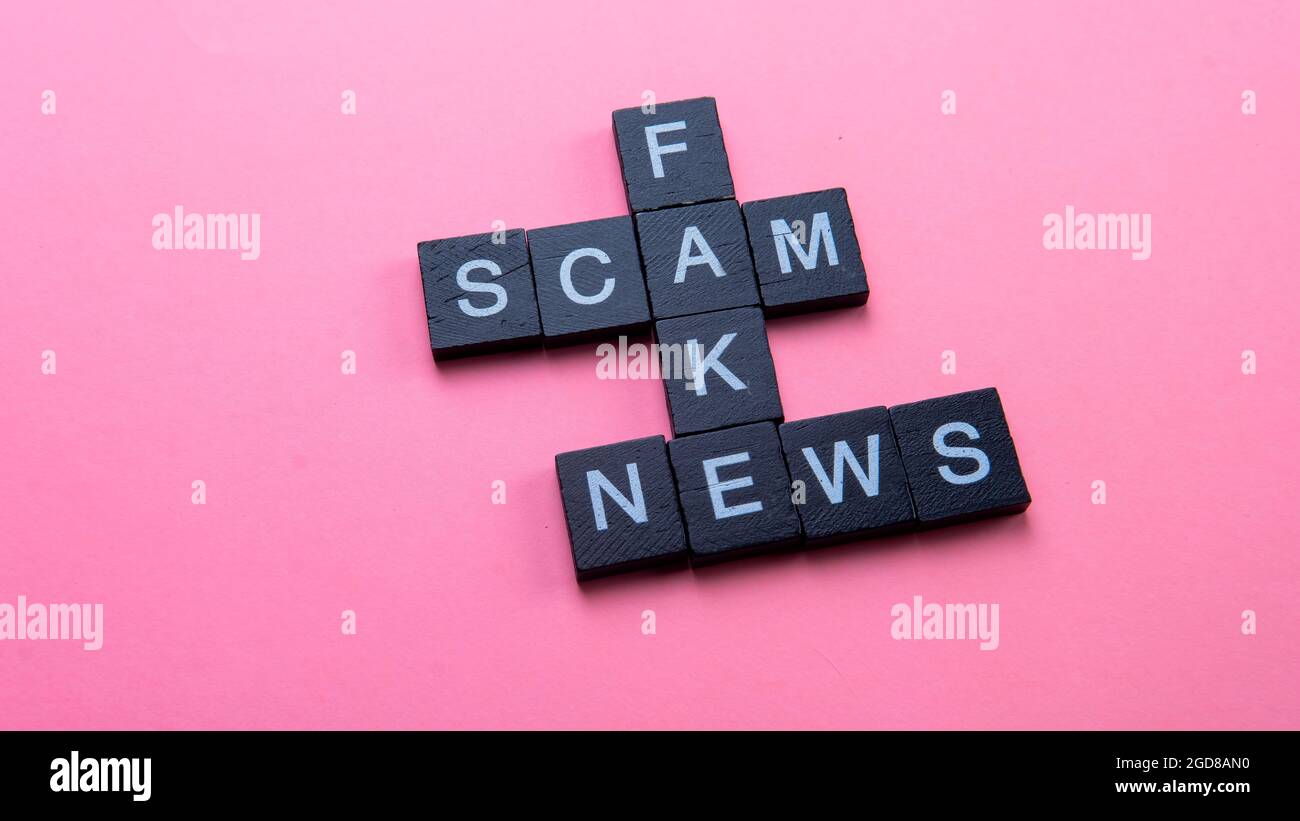 Un gruppo di piastrelle scrable che formano le notizie false di truffa di parola. Fuoco selettivo sulle piastrelle isolate su sfondo rosa Foto Stock