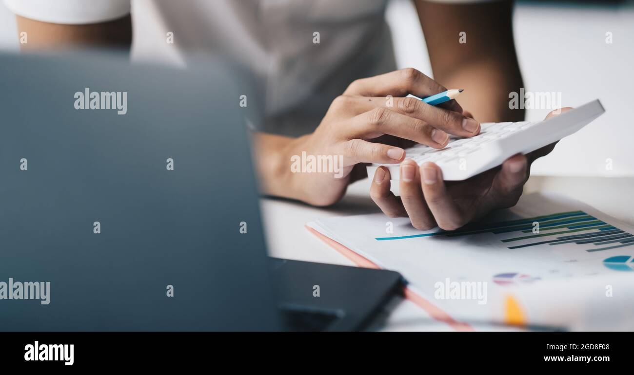 Primo piano mano del contabile che lavora sulla scrivania del luogo di lavoro in ufficio calcolatore d'uso calcola le spese mensili, le tasse, il saldo del conto corrente bancario Foto Stock