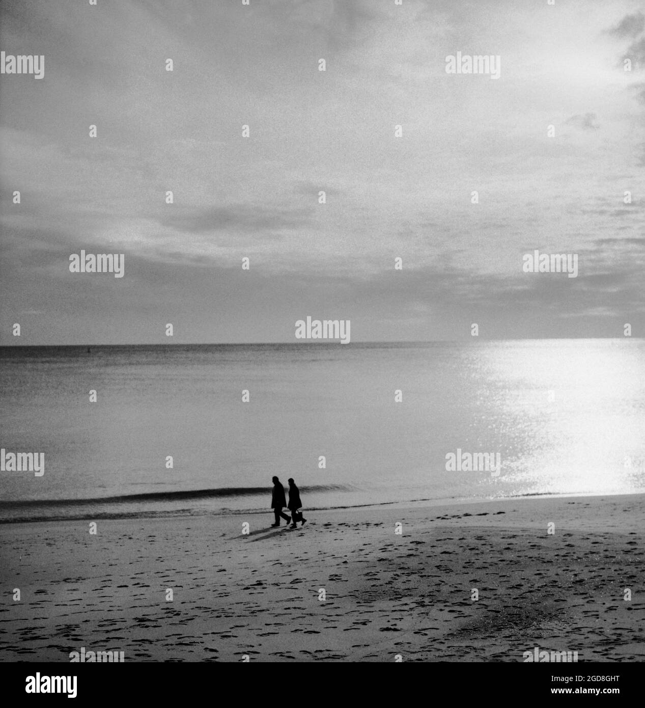 SESIMBRA, PORTOGALLO - 09 gennaio 2021: Una foto in scala di grigi di una vecchia coppia che cammina sulla spiaggia di Sesimbra, Portogallo Foto Stock