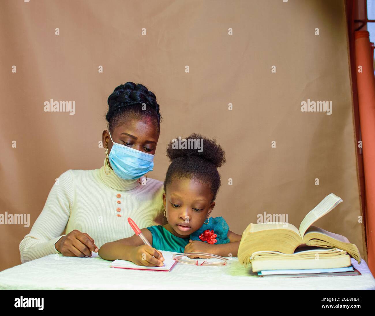 Insegnante o madre africana con maschera al naso, insegnando e aiutando una bambina con i suoi studi per eccellere nella scuola, nell'istruzione e nella carriera Foto Stock