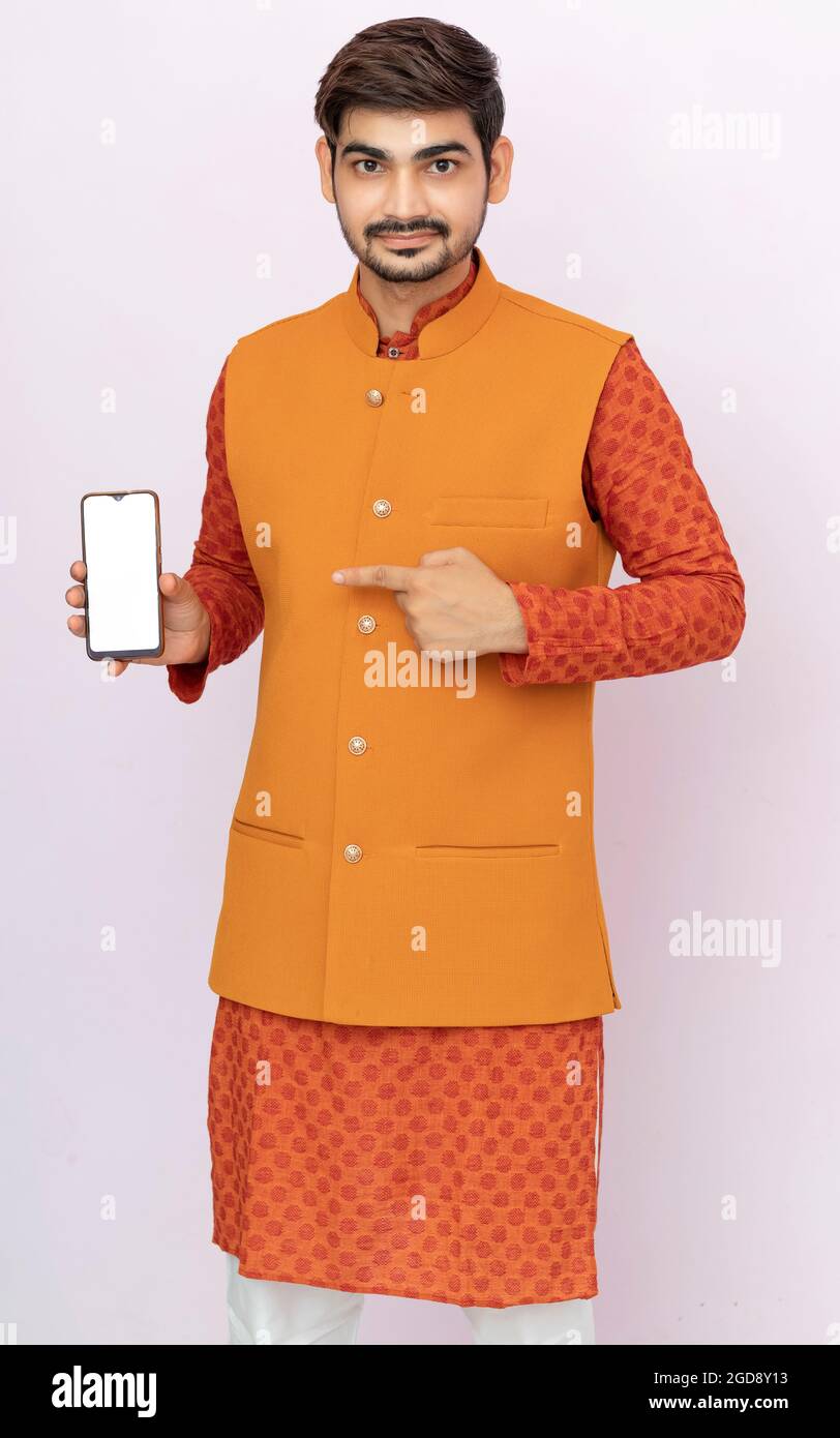 Ritratto di un giovane allegro che indossa etnico indiano tradizionale abbigliamento sfondo isolato, mostrando schermo vuoto telefono cellulare. Foto Stock