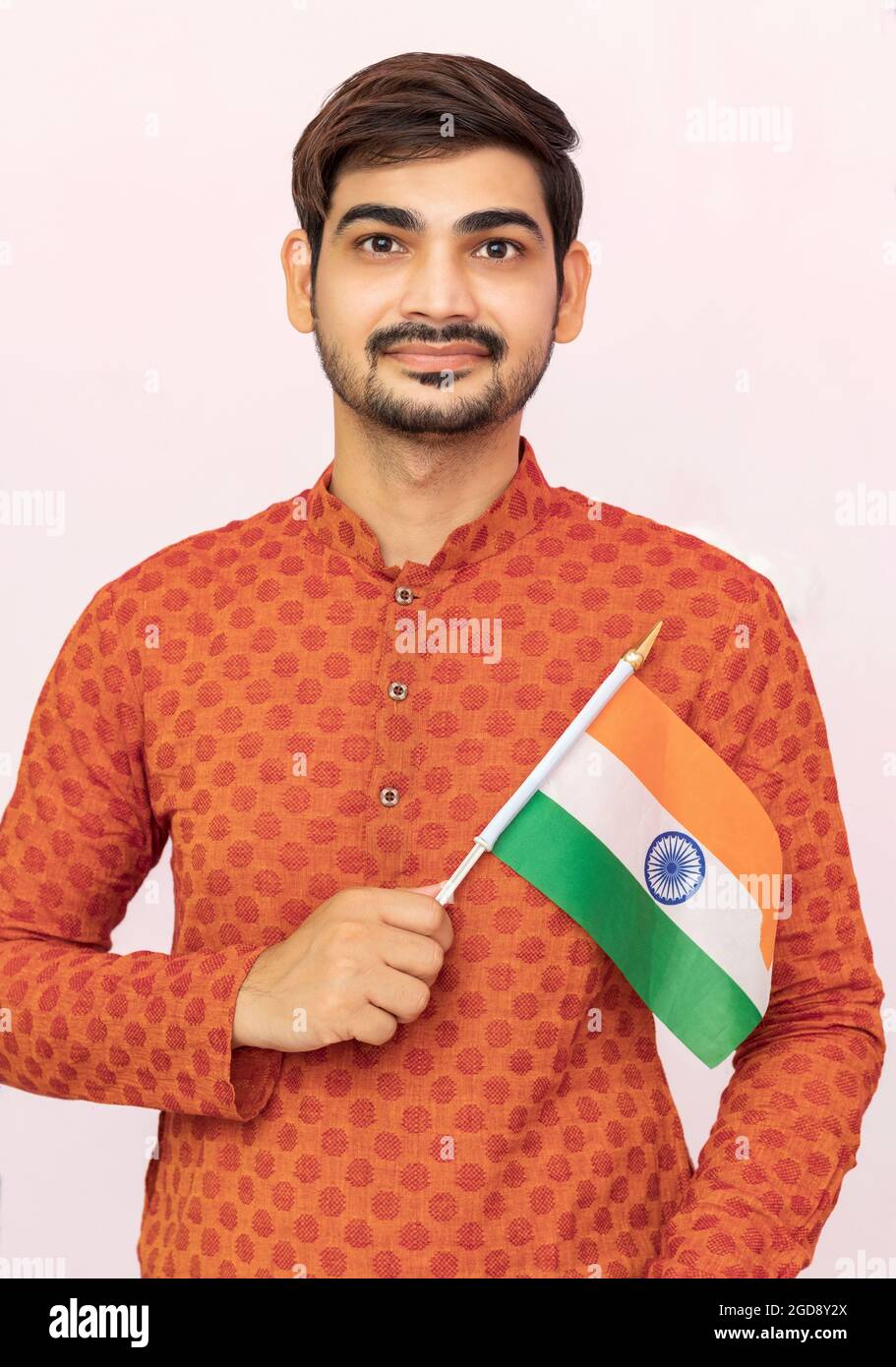 Bel ragazzo o uomo indiano in abbigliamento etnico che tiene la bandiera nazionale indiana e mostra patriottismo, in piedi su sfondo isolato. Foto Stock