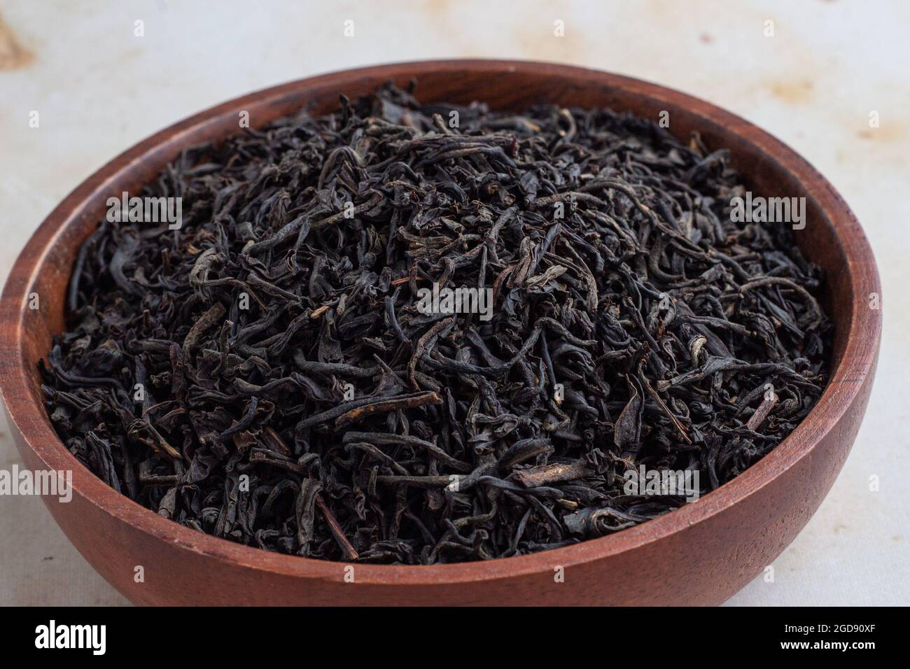 Foglie di tè Assam essiccato in una ciotola di legno Foto Stock
