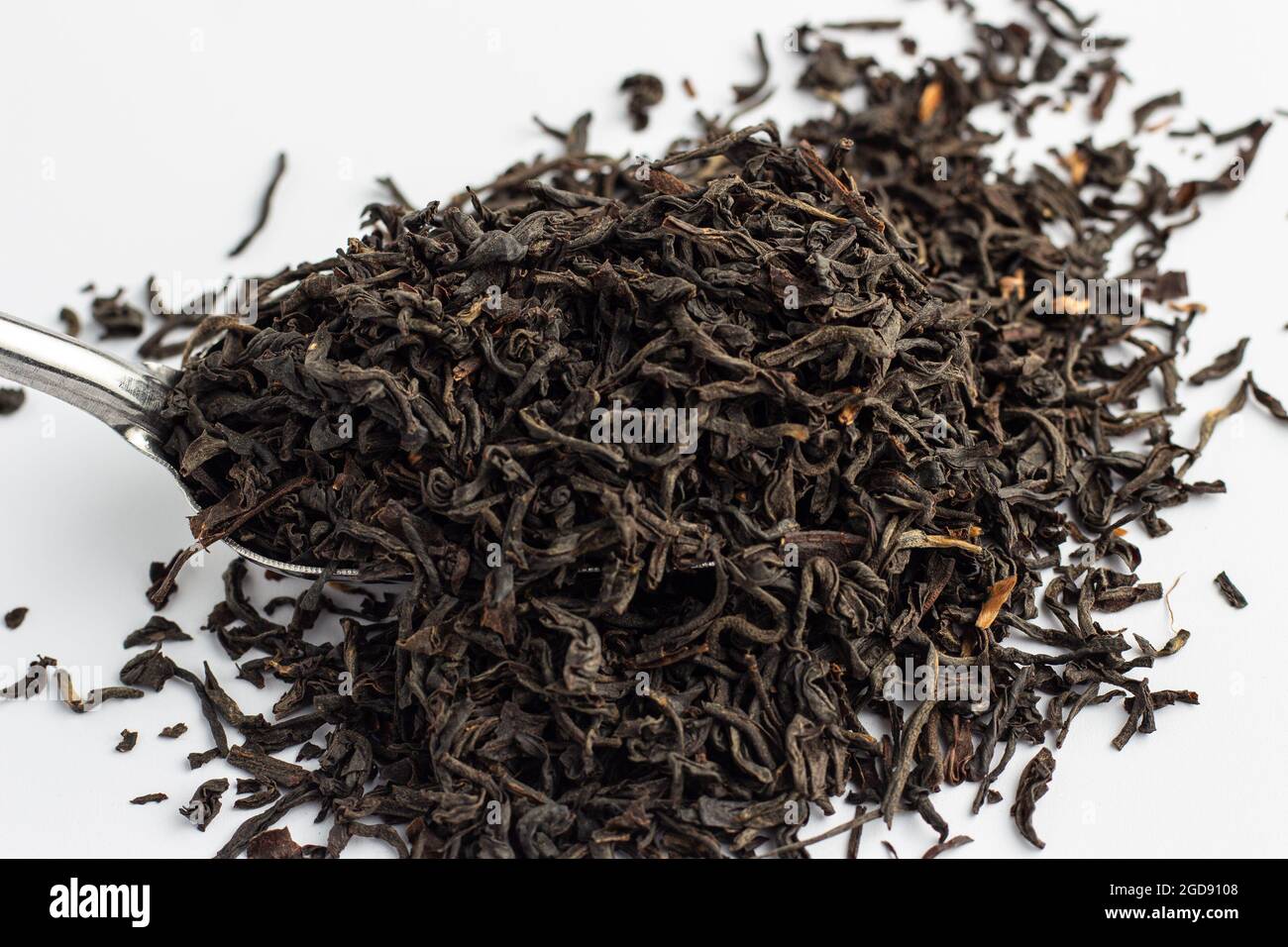 Foglie di tè Assam essiccato su cucchiaio d'argento su sfondo bianco. Foto Stock