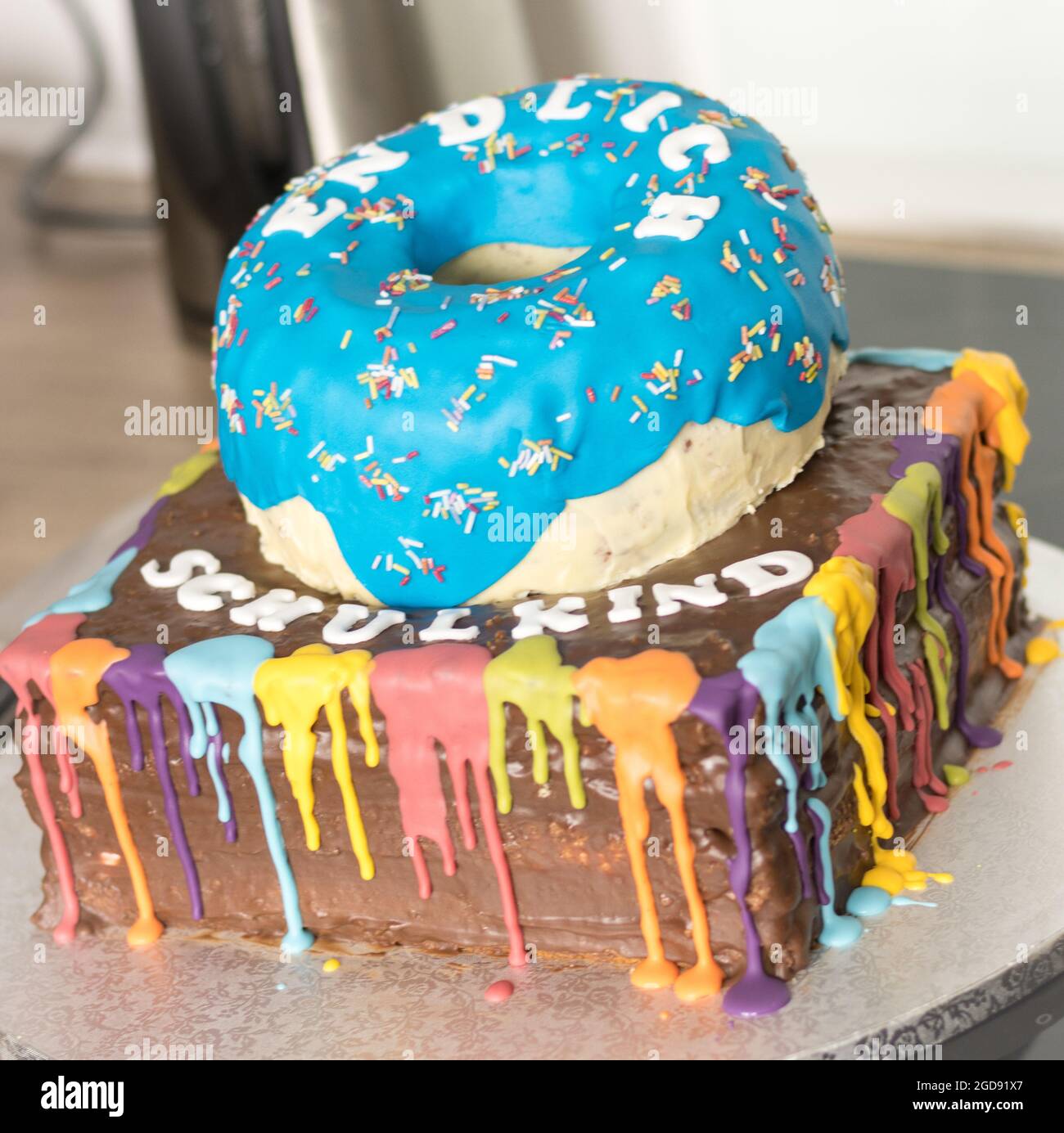 Una torta colorata caratterizzata da un design a forma di ciambella blu, con una brillante glassa arcobaleno e il testo "Schulkind", che celebra un'occasione speciale. Foto Stock