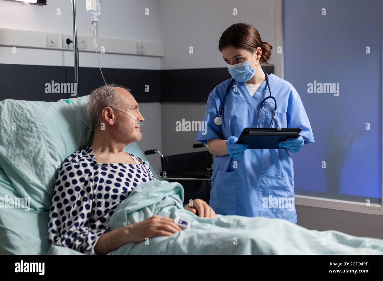 Medico afroamericano con maschera chirurgica in sala d'ospedale che discute diagnosi e trattamento con l'uomo anziano malato che si posa a letto rassicurando il recupero completo. Paziente malato che respira attraverso la maschera di ossigeno. Foto Stock