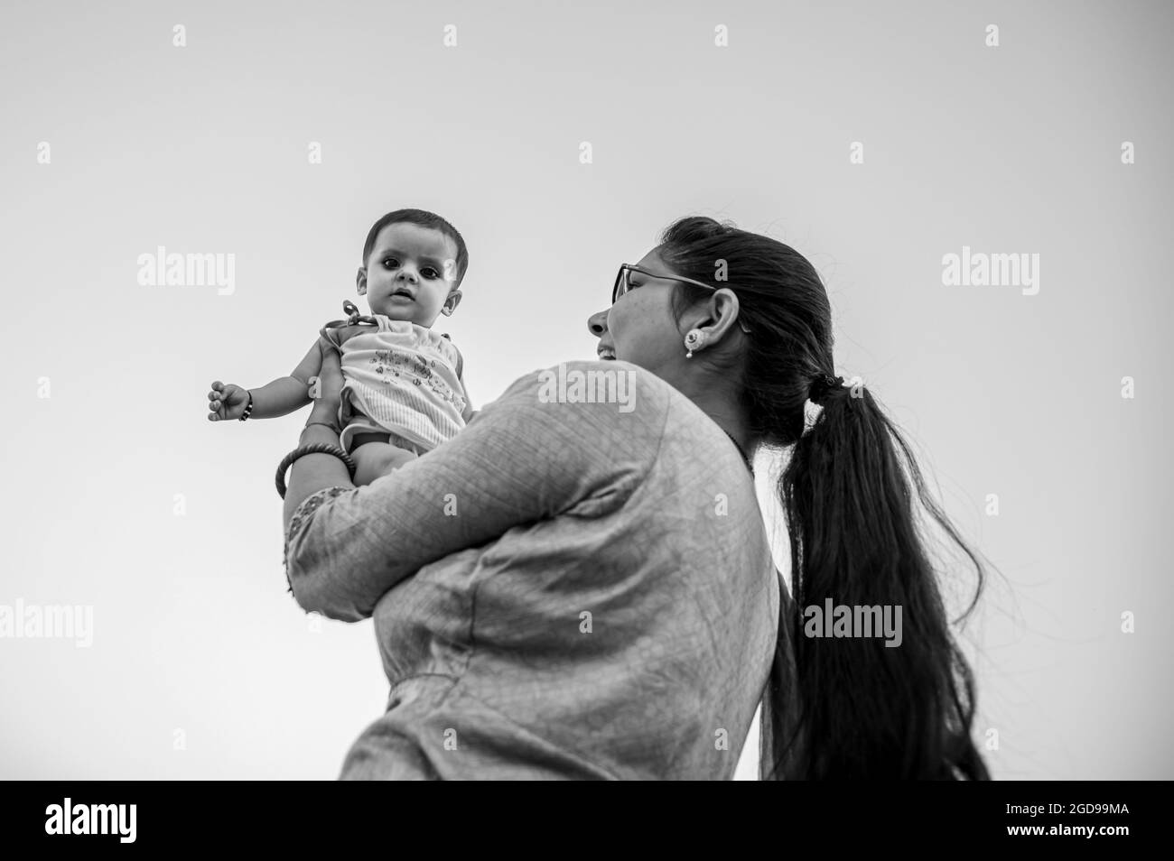 ritratto di madre indiana che solleva e gioca con il neonato, emozioni umane positive, sfondo di famiglia. Foto Stock