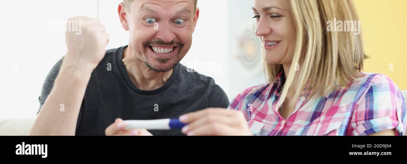 L'uomo e la donna gioiscono e tengono test di gravidanza positivo a casa Foto Stock