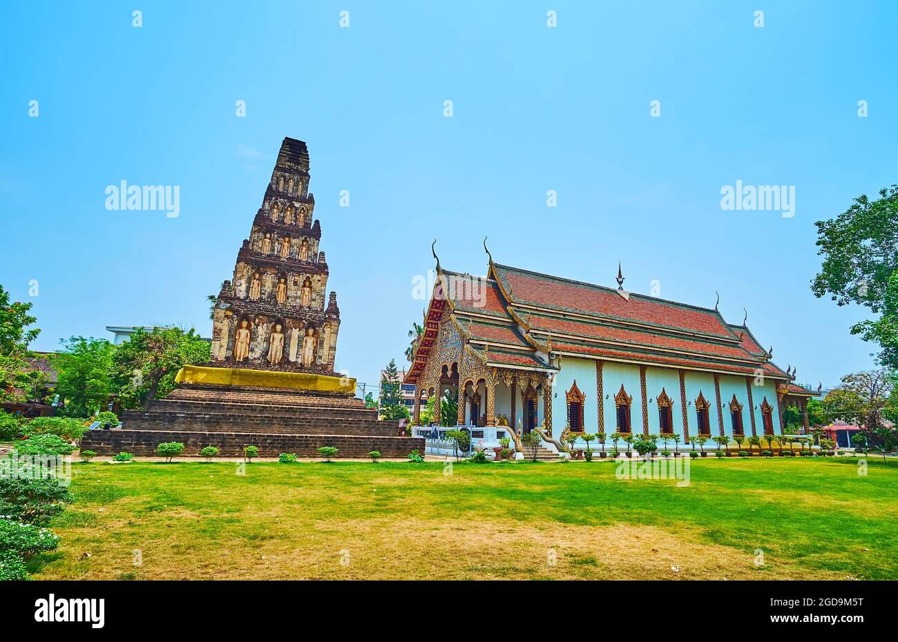 La scenografica Sala Viharn del Tempio di Wat Chammathewi con tetto a timpano, decorazioni intagliate ornate e la stupa Suwan Chedi Jungkote accanto ad esso, Lamphun, Th Foto Stock