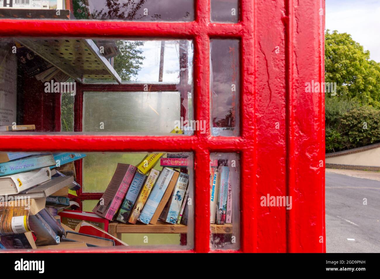 Guardando attraverso la finestra di una scatola telefonica pubblica decommissionata ora ha utilizzato una libreria Foto Stock