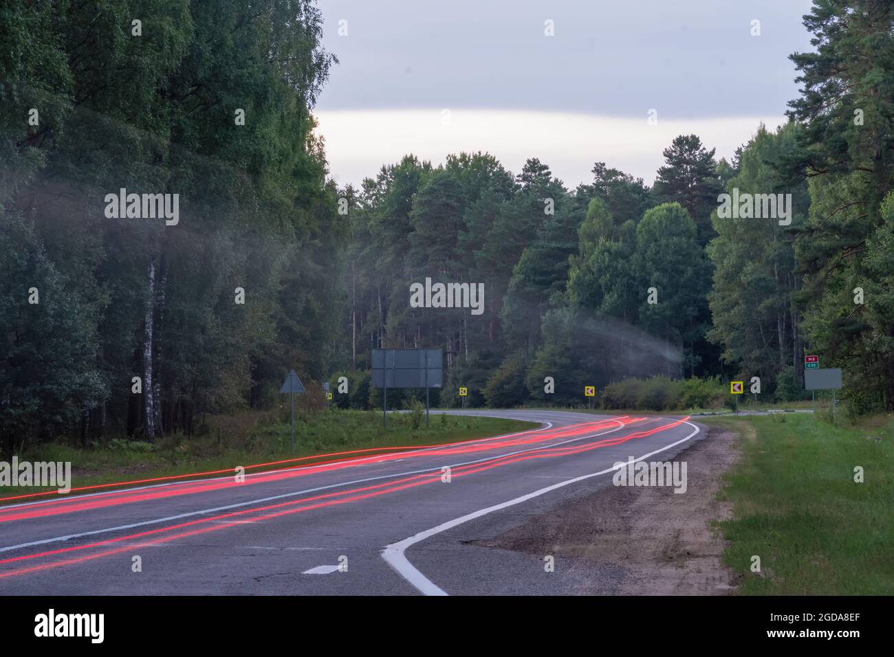 Passando l'auto sulla strada nella foresta con una svolta su una lunga velocità di scatto. Condizioni di guida potenzialmente pericolose Foto Stock