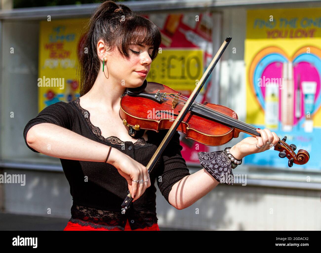 Dundee, Tayside, Scozia, Regno Unito. 12 agosto 2021. Regno Unito tempo: Una calda giornata ventosa con abbondante sole in tutto il Nord-Est della Scozia con temperature che raggiungono i 18°C. Una giovane violinista alla moda che suona musica classica mentre si porta fuori dal centro commerciale Overgate di Dundee. Credit: Dundee Photographics/Alamy Live News Foto Stock