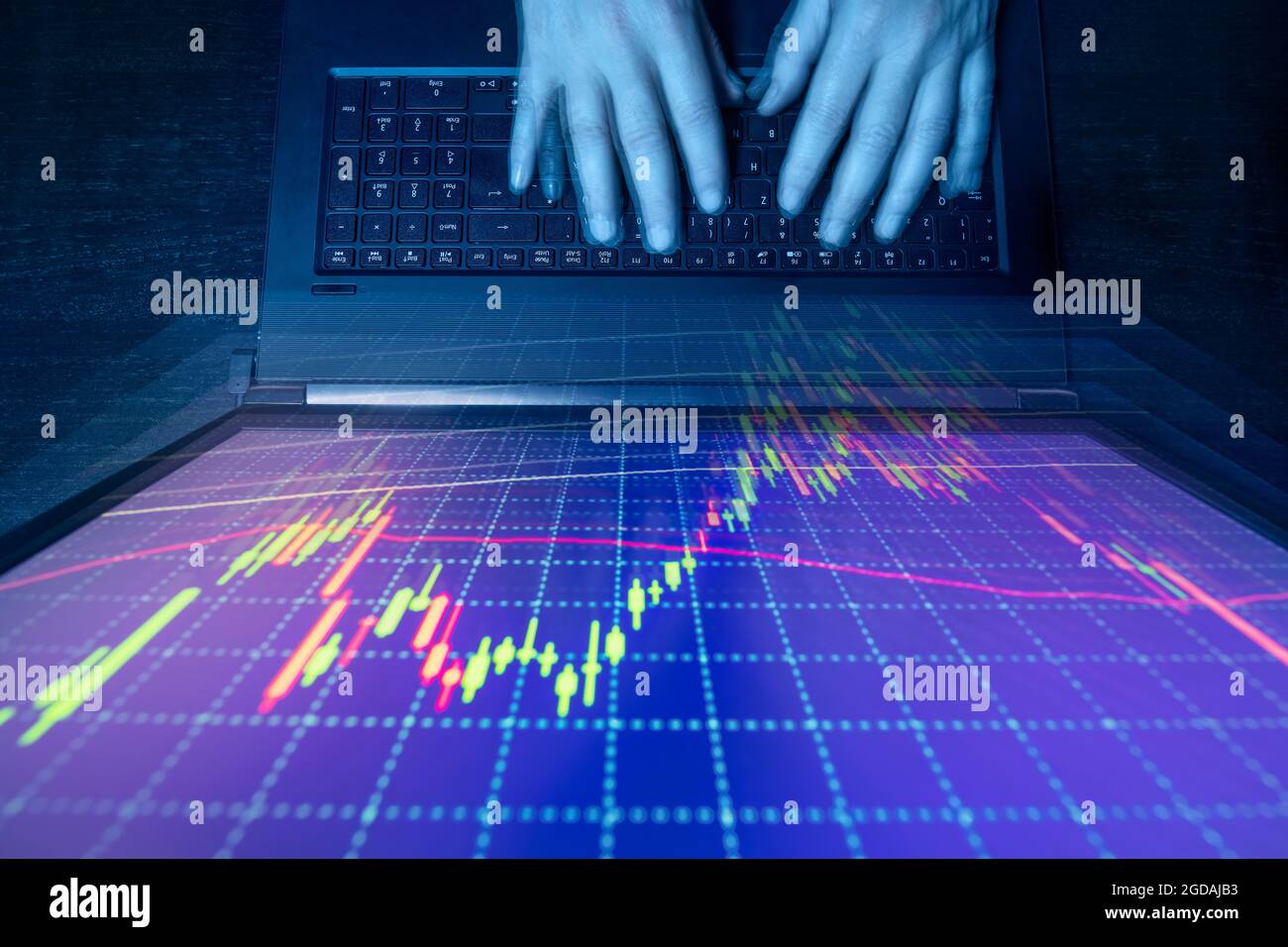 Computer e monitor con grafico finanziario in vista dall'alto e ambiente oscuro Foto Stock
