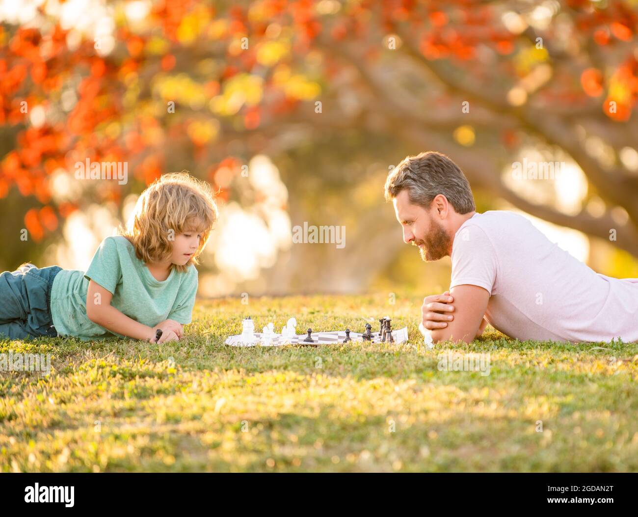 famiglia felice di papà e figlio capretto che gioca a scacchi su erba verde nel parco all'aperto, genio Foto Stock