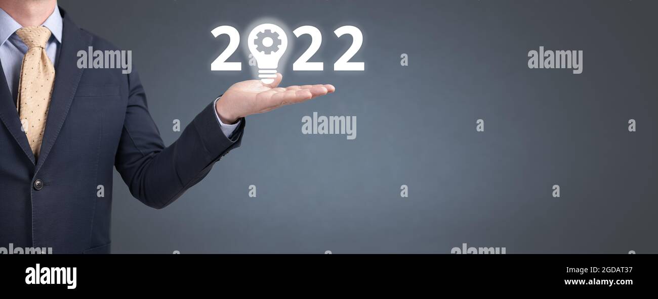 L'uomo d'affari tiene l'anno 2022 con il simbolo dell'innovazione sulla sua mano. Nuovo anno 2022 e lampadina su sfondo grigio blu con spazio di copia per il nuovo Foto Stock