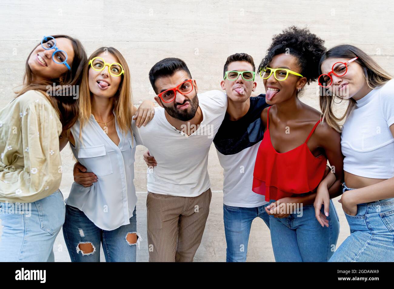 Interrazziale gen z giovani che si divertono a fare i volti strani e indossare occhiali colorati. Foto Stock