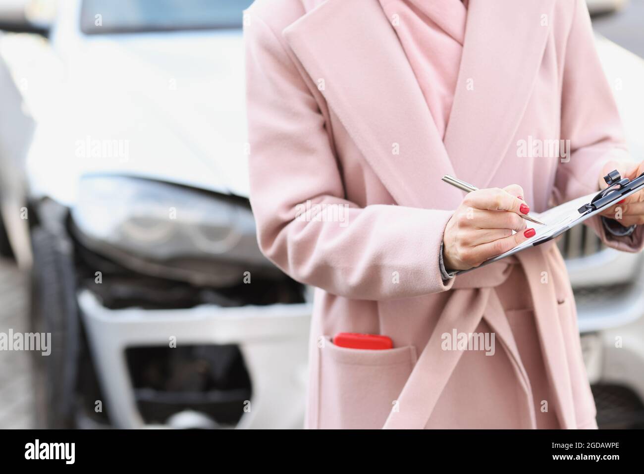 Donna in cappotto che compila i documenti sullo sfondo di auto rotto closeup Foto Stock