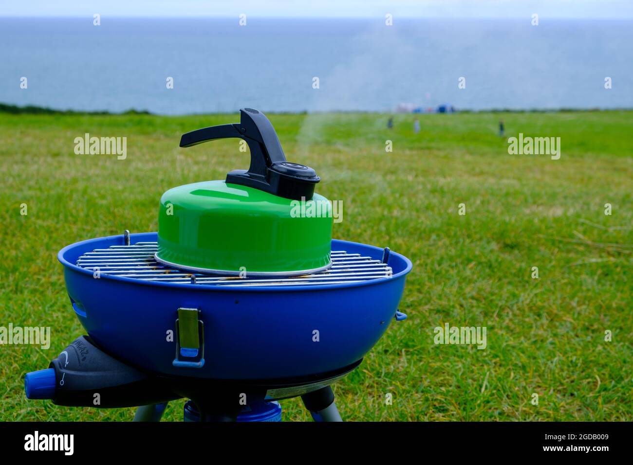 Stufa da campeggio Blue Campingaz con bollitore bollente verde con vapore  che esce dal beccuccio e il mare sullo sfondo.2021 Foto stock - Alamy