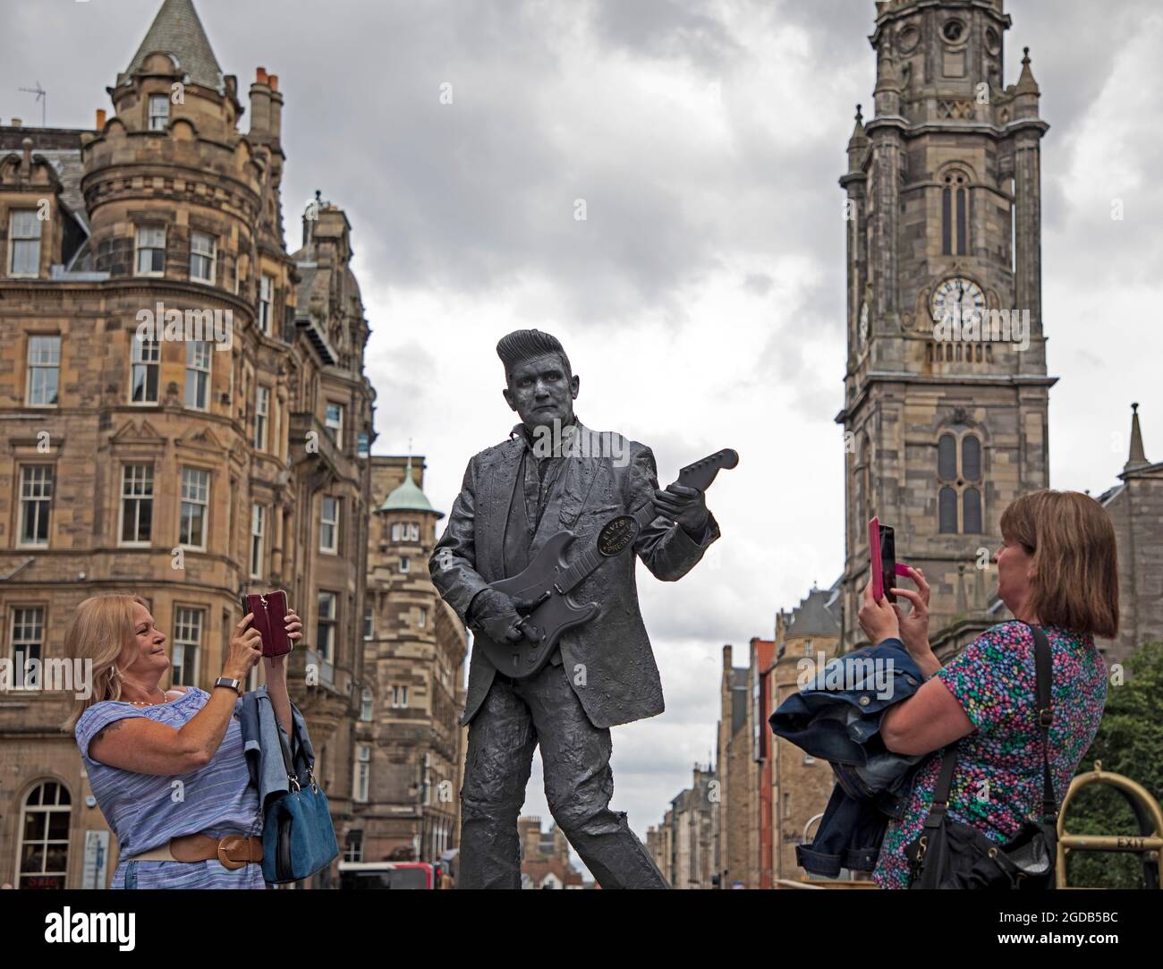 Royal Mile, Edimburgo, Scozia, Regno Unito. 12 agosto 2021. Edinburgh Fringe Festival, il settimo giorno della serata sulla capitale High Street evento. Tempo arioso e nuvoloso con una temperatura di 18 gradi per le statue umane e gli artisti di strada che attirano la folla sulle loro piazzole. Nella foto: Elvis è arrivato al Fringe aka. Kevin Powell, Human statue divertente passanti su High Street, Susan e Lorraine in visita dai confini scozzesi erano ansiosi di scattare una foto sui loro telefoni cellulari. Credit: Arch White/Alamy Live News Foto Stock