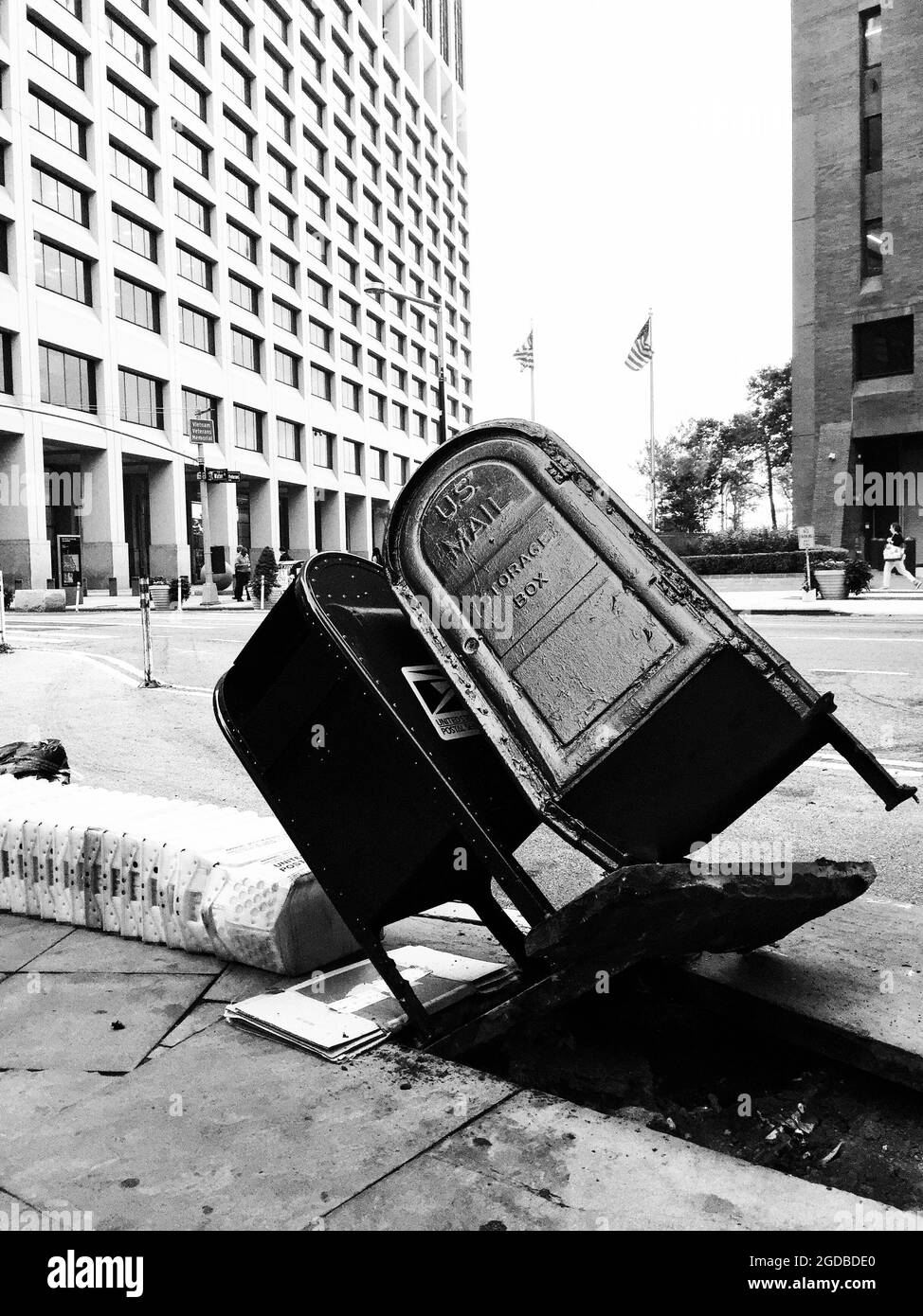 Appoggiando le scatole di posta degli Stati Uniti, blocco di cemento del marciapiede tirato su da che cosa deve essere stato un momento di incidente. Girato in bianco e nero, forte, contrasty. Foto Stock
