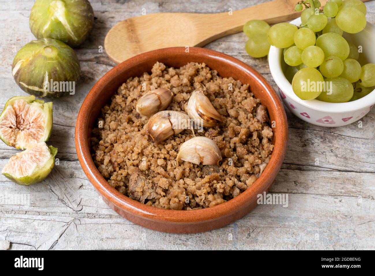 Primo piano di un tipico piatto spagnolo chiamato Migas, accompagnato da uve e fichi, su un rustico fondo ligneo. Foto Stock