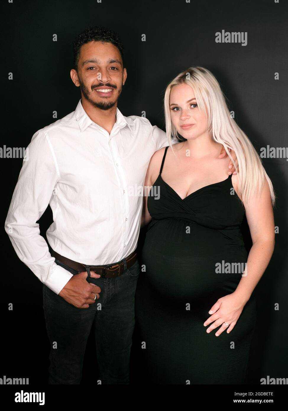 Ritratto verticale di una coppia multietnica elegante e felice che si aspetta un bambino che si tiene l'un l'altro Foto Stock