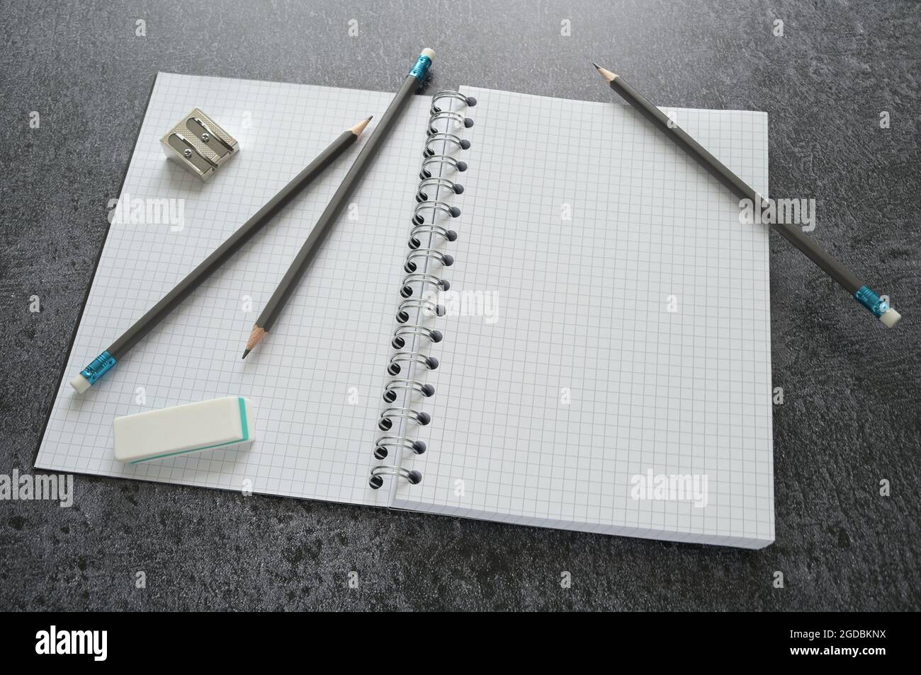 Desktop di lavoro con un notebook vuoto a spirale aperta, matite, affilatrice e cancellatrice su un tavolo grigio scuro, mock-up con spazio di copia, messa a fuoco selezionata, stretta Foto Stock