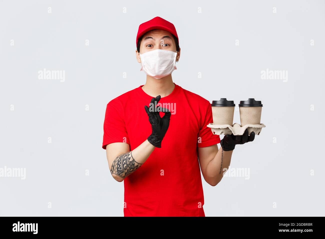 Il tuo ordine è sicuro con i nostri corrieri. Carismatico addetto alla consegna in uniforme rossa e maschera medica, guanti, bevande in attesa, portare l'ordine alla porta del cliente Foto Stock