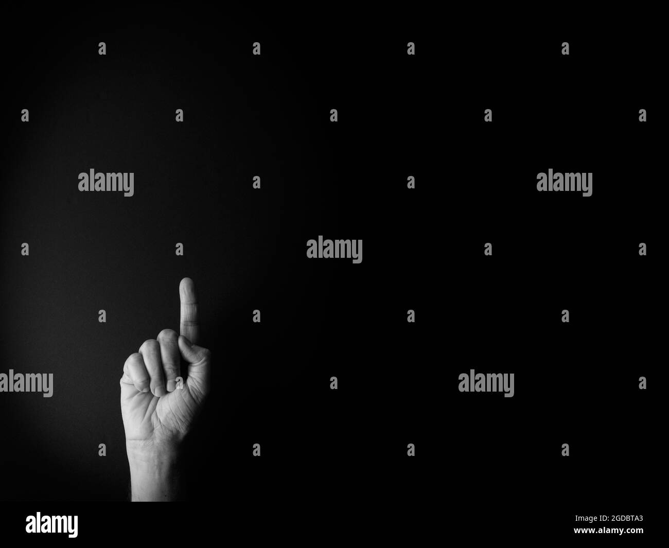 Immagine drammatica in bianco e nero della mano maschile che mostra il numero uno del linguaggio dei segni su sfondo nero con spazio vuoto per i redattori Foto Stock