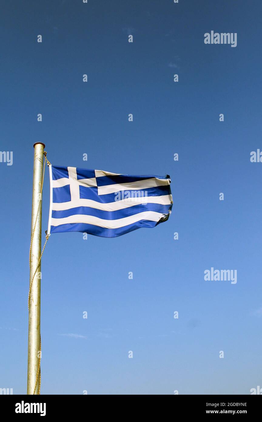 Bandiera greca che batte nella brezza, isola di Sikinos, Grecia. Scatto verticale con sfondo blu. Spazio di copia. Foto Stock