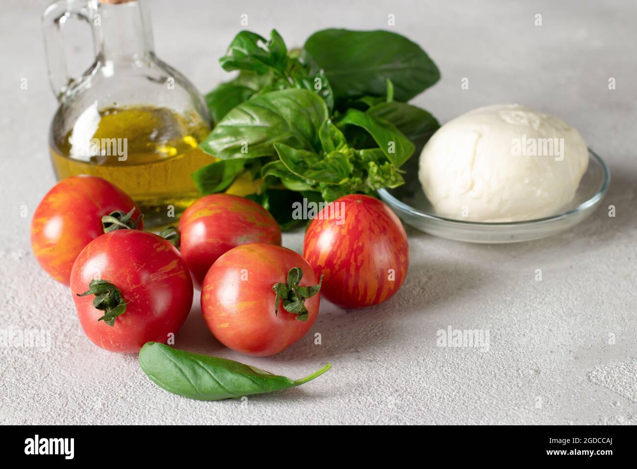 Ingredienti per la preparazione dell'insalata caprese: Pomodori, mozzarella, basilico e olio d'oliva su sfondo grigio chiaro. Primo piano Foto Stock