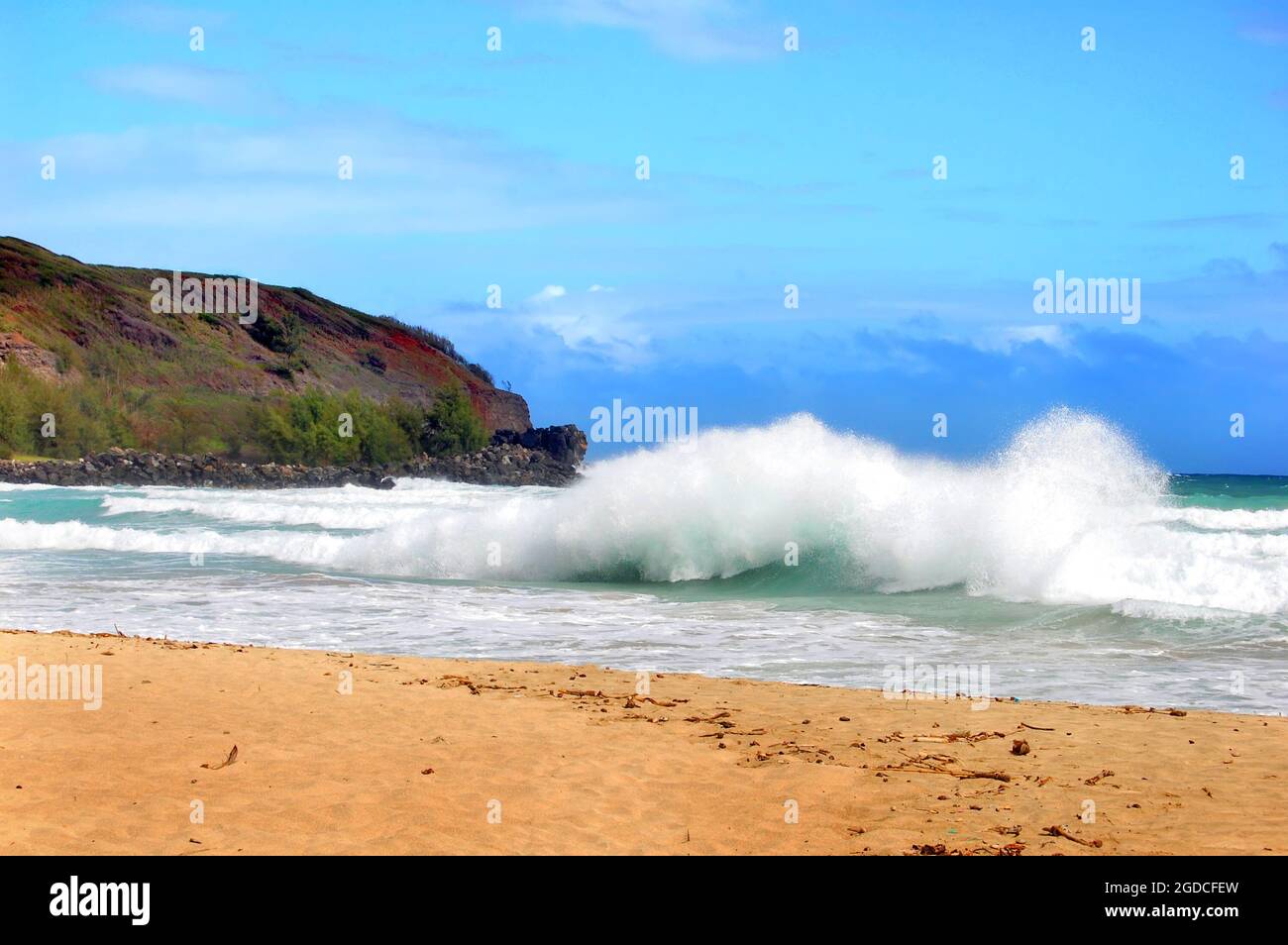 Una grande onda si tuffa verso la riva su una spiaggia deserta sull'isola di Kauai, Hawaii. I cieli sono blu e acqua acqua. Foto Stock