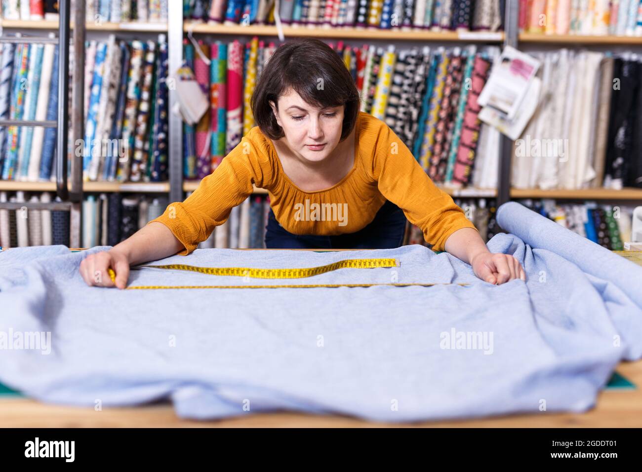 Venditore che misura e taglia il pezzo di stoffa Foto Stock