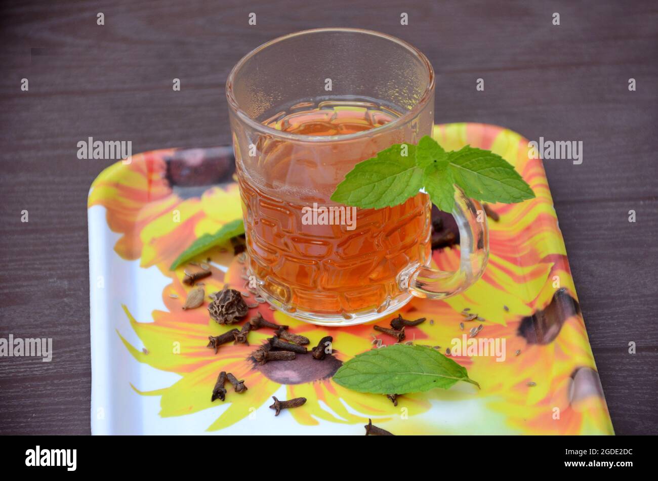 nella tazza di vetro, preparare il tè marrone nero con chiodi di garofano neri, pepe nero, finocchio e menta verde su sfondo marrone fuori fuoco. Foto Stock