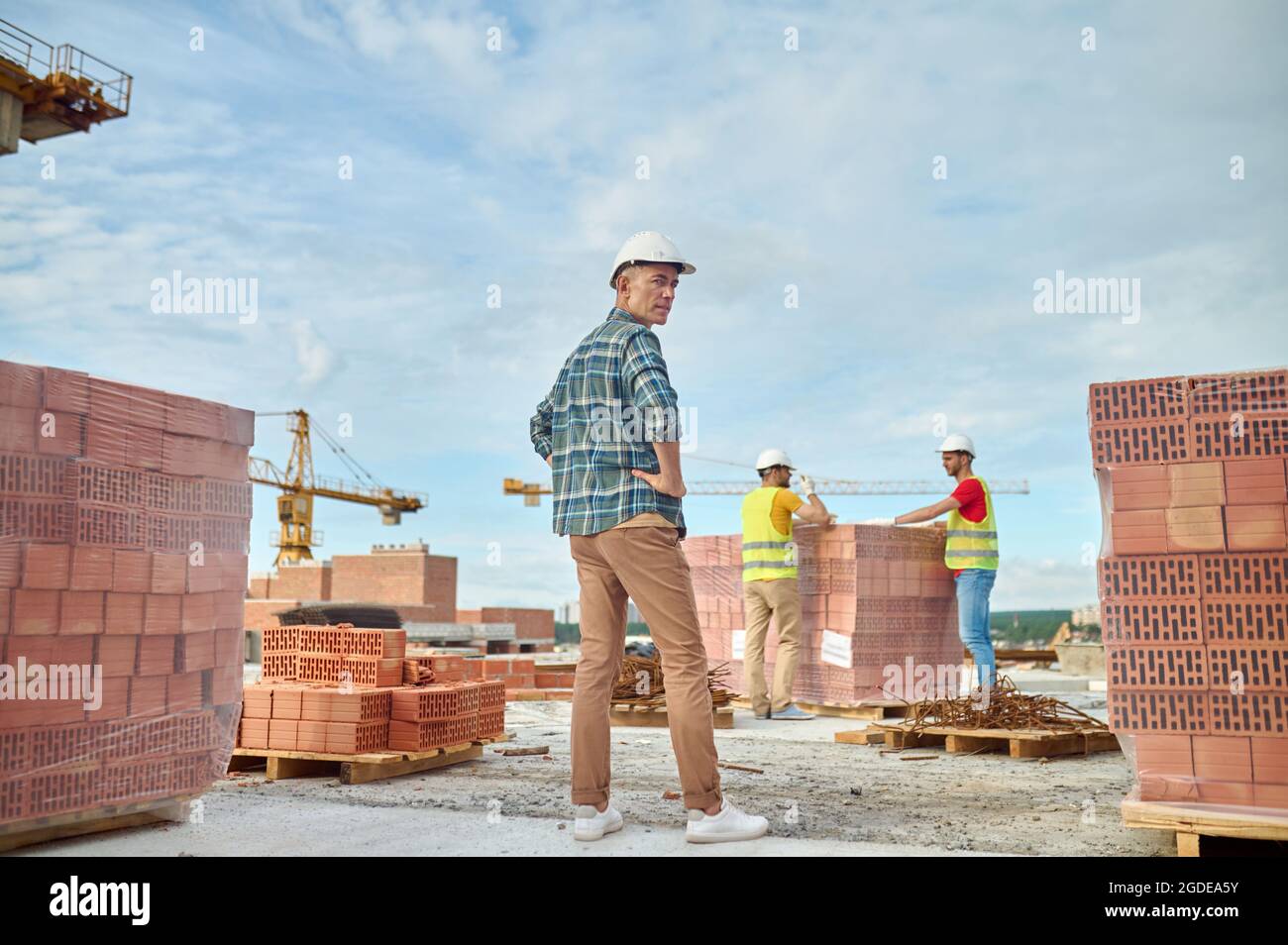 Tre operai di costruzione fra i mattoni forati rossi impilati Foto Stock