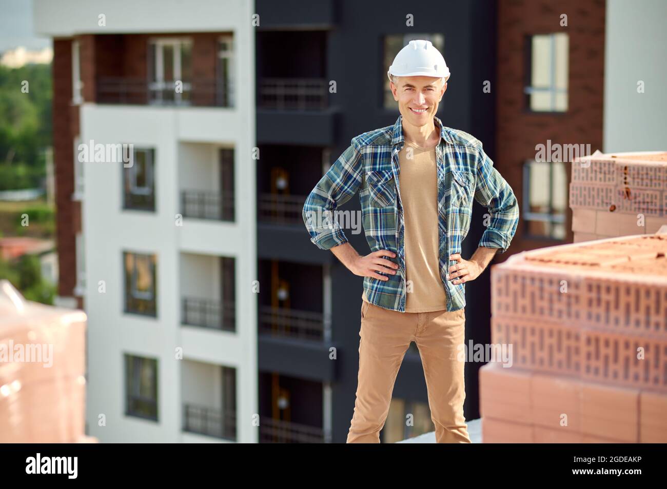 Gioioso lavoratore attraente in un hardhat in cima a un edificio costruito a metà Foto Stock