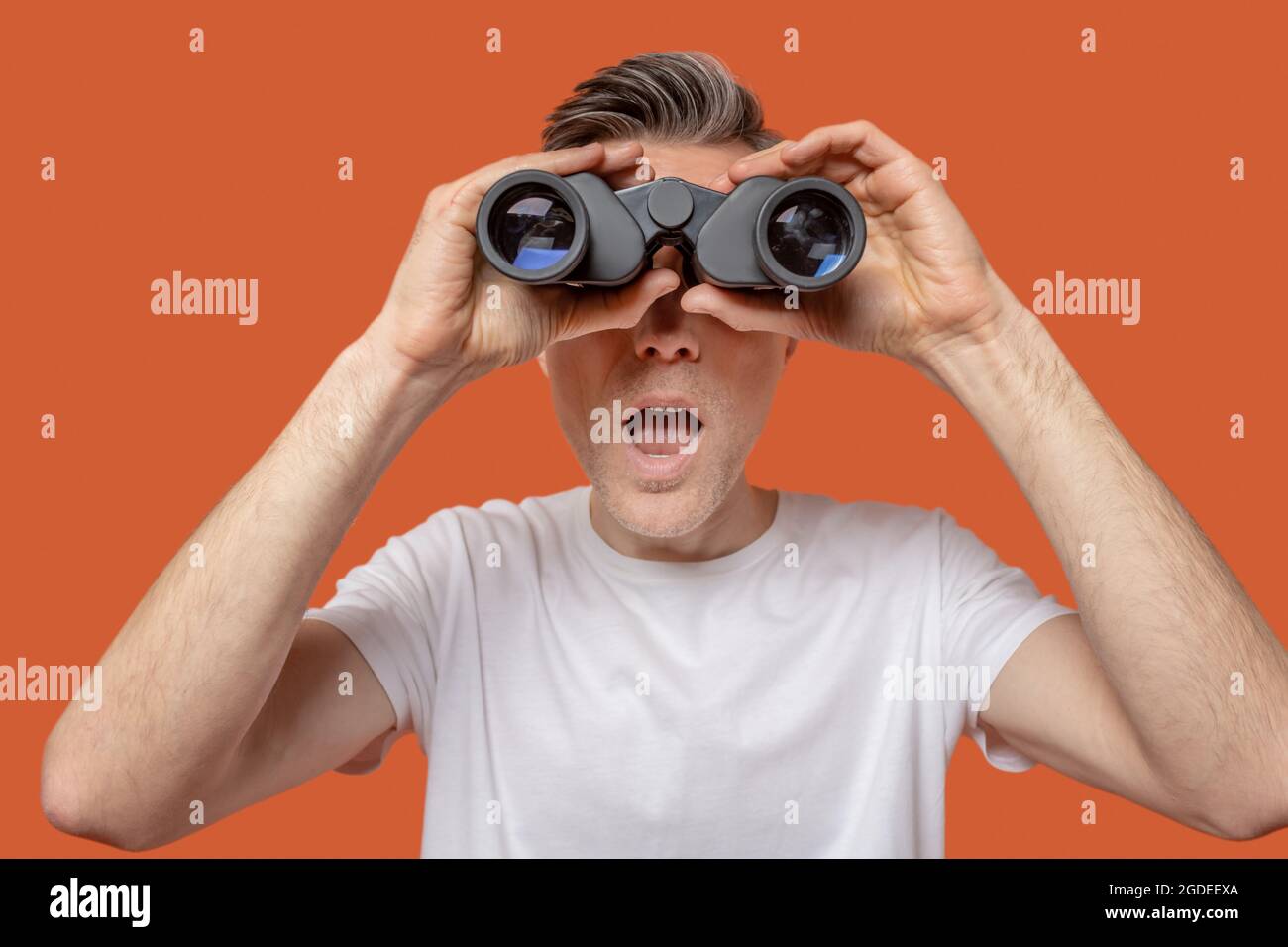 Uomo che guarda attraverso binocoli con bocca aperta Foto Stock