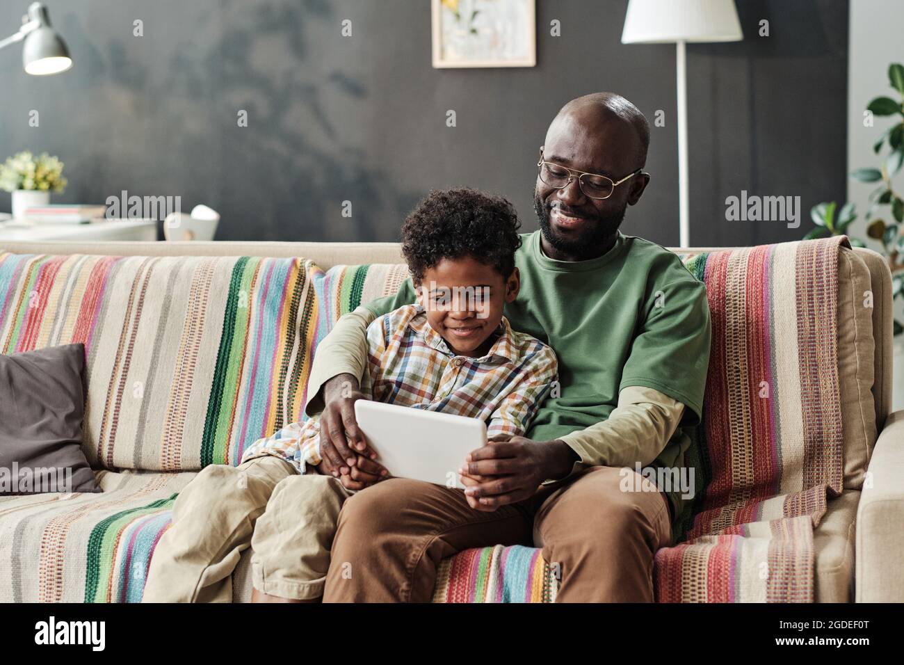 Felice padre africano seduto sul divano e giocare online su tablet digitale insieme con suo figlio a casa Foto Stock