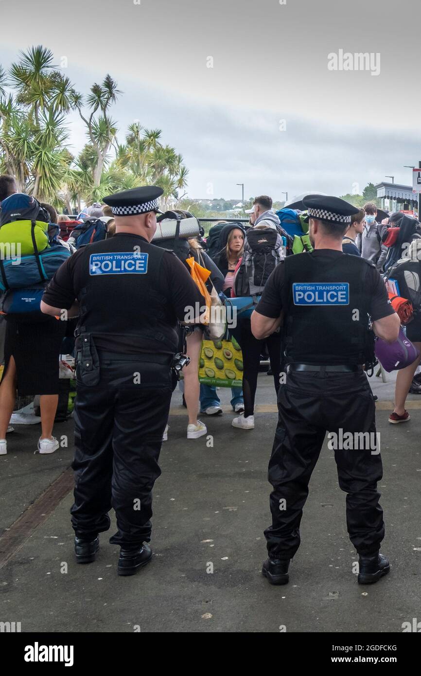 La polizia guarda i giovani che arrivano alla stazione ferroviaria di Newquay per il giorno di apertura del Boardmasters Festival in Cornovaglia. Foto Stock