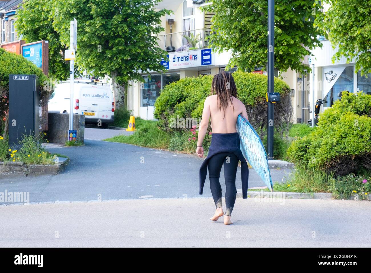 Un surfista che torna a casa portando la sua tavola da surf e camminando attraverso la città di Newquay in Cornovaglia. Foto Stock