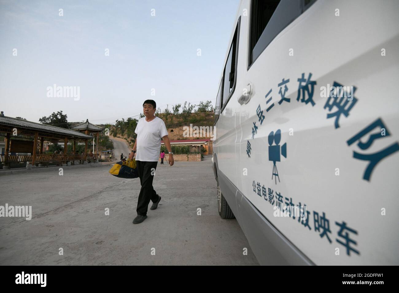 (210813) -- TAIYUAN, 13 agosto 2021 (Xinhua) -- Liu Bufei passa davanti a un'auto mobile di proiezione del film con lo schermo in mano nel villaggio di Gaojiayan, Sanjiao Township della contea di Liulin, nella provincia di Shanxi, 10 agosto 2021. Nel 1975, Sanjiao Township fondò un team di proiezione cinematografica. Liu Bufei e Liu Dengzhao, entrambi cinefili fin dall'infanzia, si unirono alla squadra e divennero proiettisti rurali. Nel 2007, la squadra divenne una troika con l'ingresso del proiettile di seconda generazione Xue Xiaogang, che aveva visto film all'aperto nel villaggio mentre era cresciuto. Nel corso degli anni, il team di proiezione Foto Stock