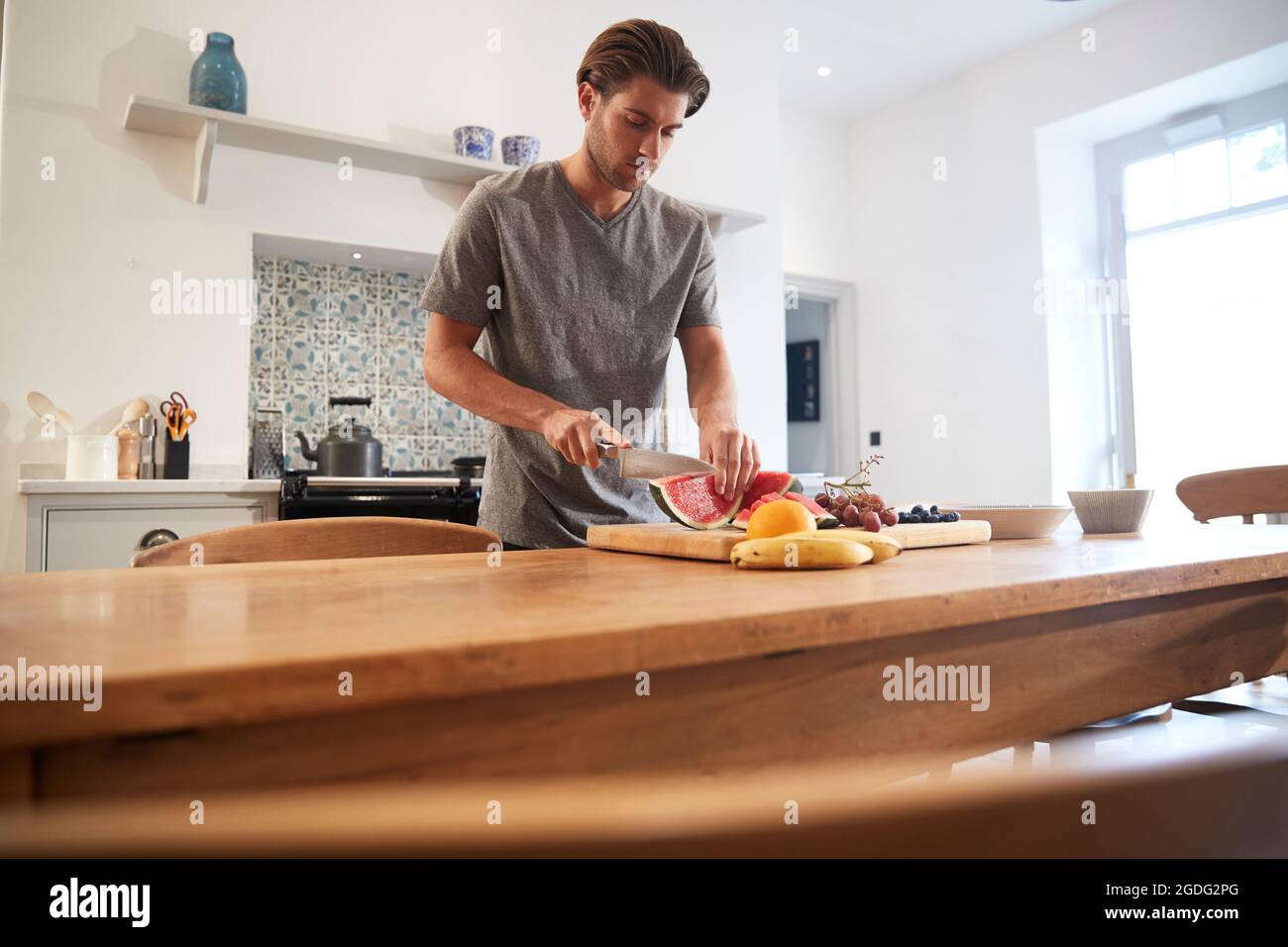 Giovane uomo per affettare cocomero fresco al tavolo della cucina Foto Stock