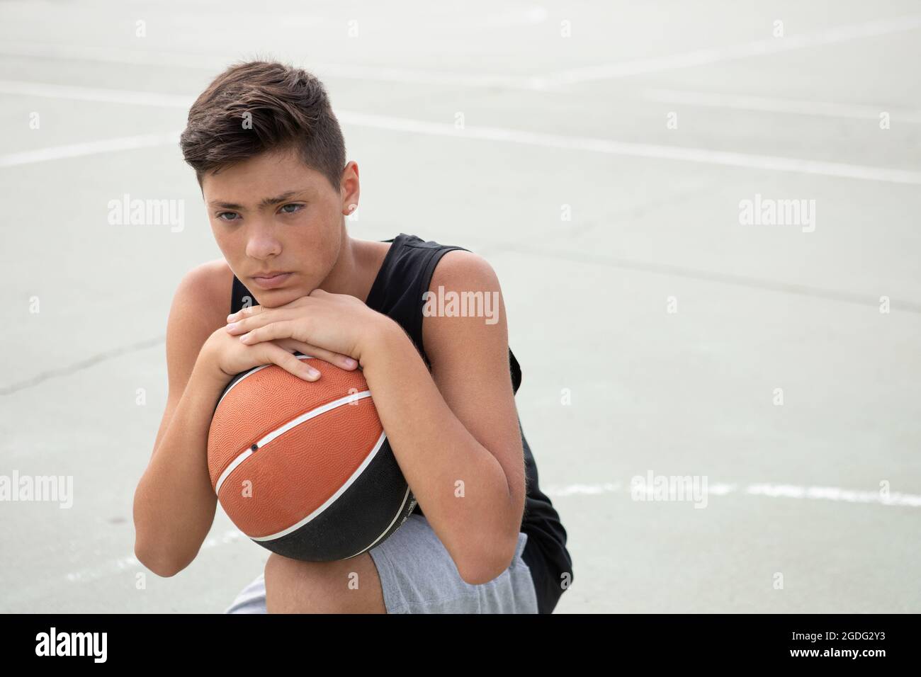 Un adolescente di sesso maschile del giocatore di basket accovacciato con la palla sul campo di pallacanestro, ritratto Foto Stock