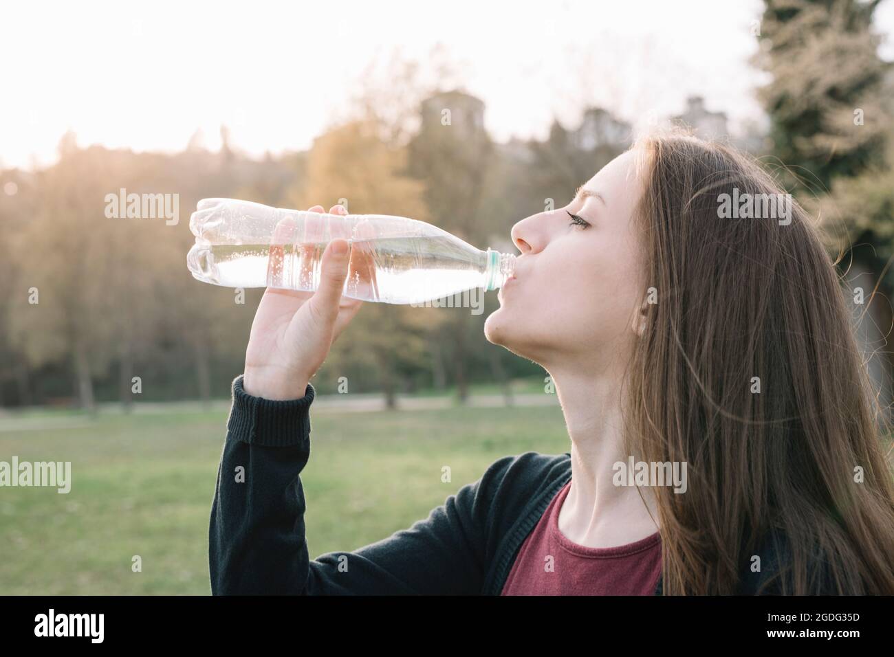 Giovane donna da bere acqua in bottiglia in posizione di parcheggio Foto Stock