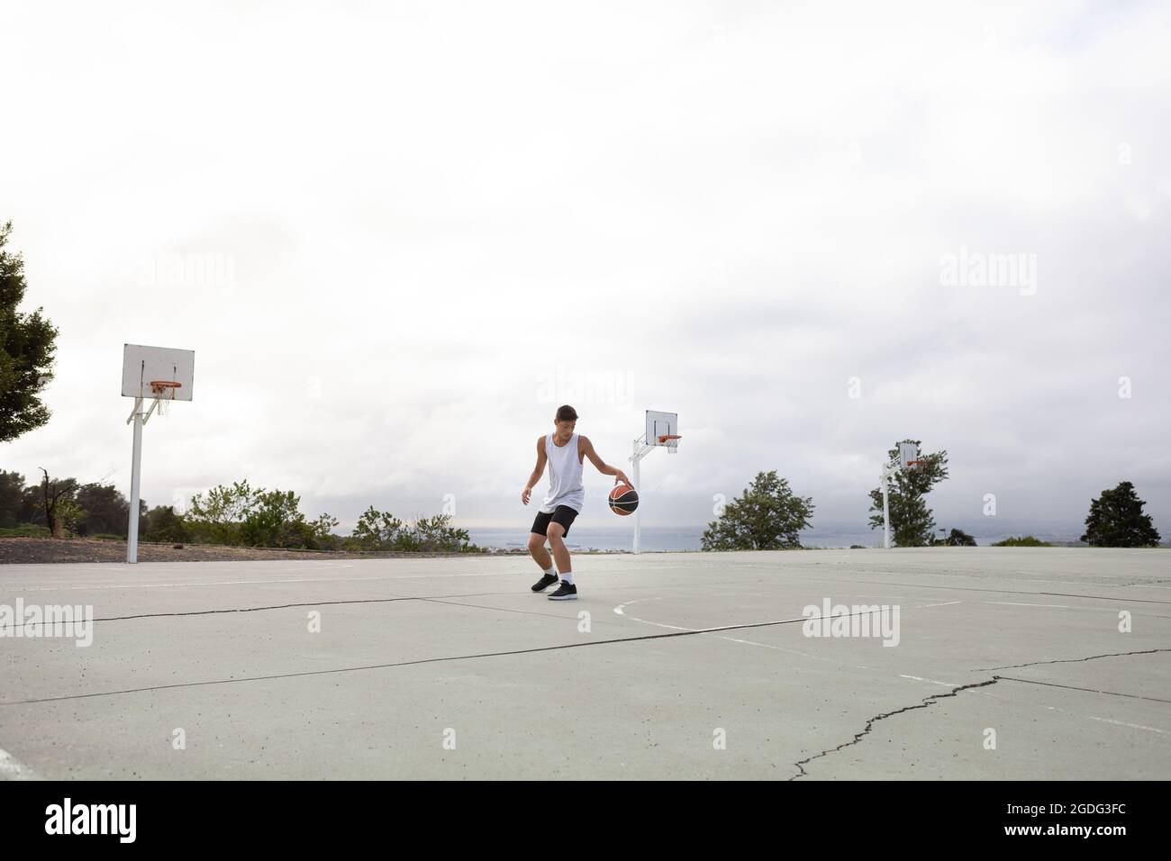 Un adolescente di sesso maschile del giocatore di basket pratica con la palla sul campo di pallacanestro Foto Stock