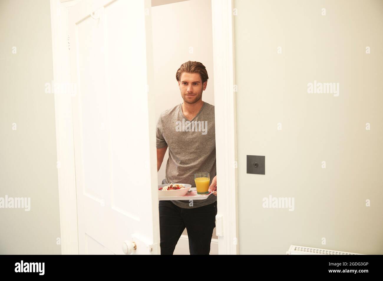 Giovane uomo che porta vassoio di prima colazione in camera da letto Foto Stock