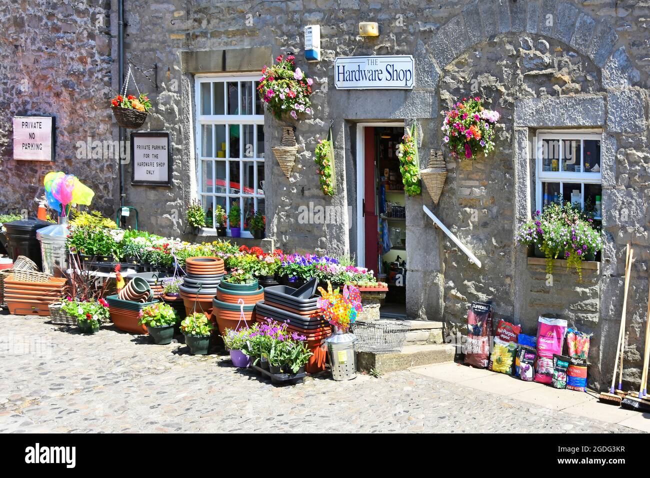 Summertime pot cresciuto estate fiori e articoli da giardinaggio fuori pietra muro hardware negozio commercio Grassington Wharfedale Yorkshire Inghilterra Foto Stock