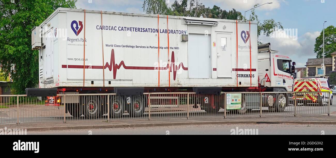 Escort van aiuta autocarro articolato hgv camion e rimorchio con carico largo un edificio portatile laboratorio di cateterizzazione cardiaca nel centro di Rugby Regno Unito Foto Stock